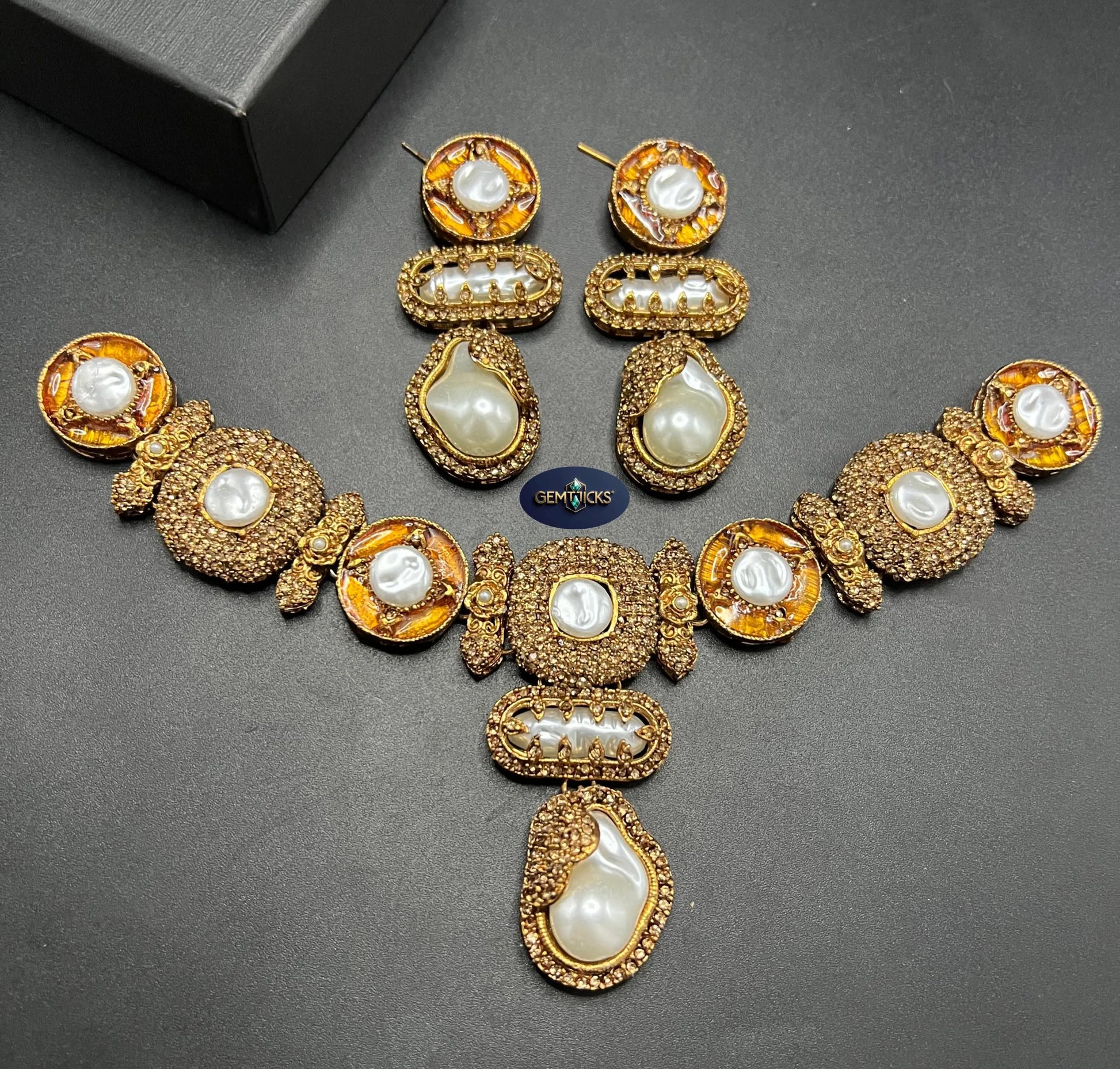 Gold necklace with pearls and matching earrings on a dark surface