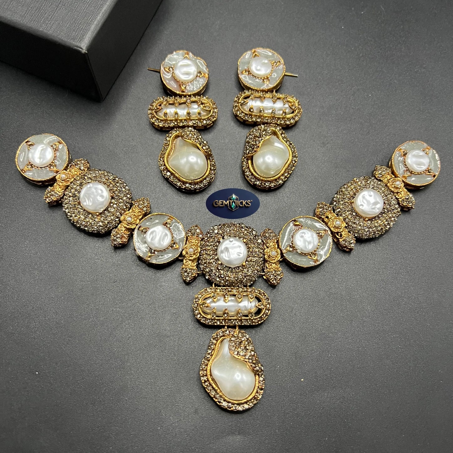 Gold and pearl jewelry set on a dark surface with a visible brand label.