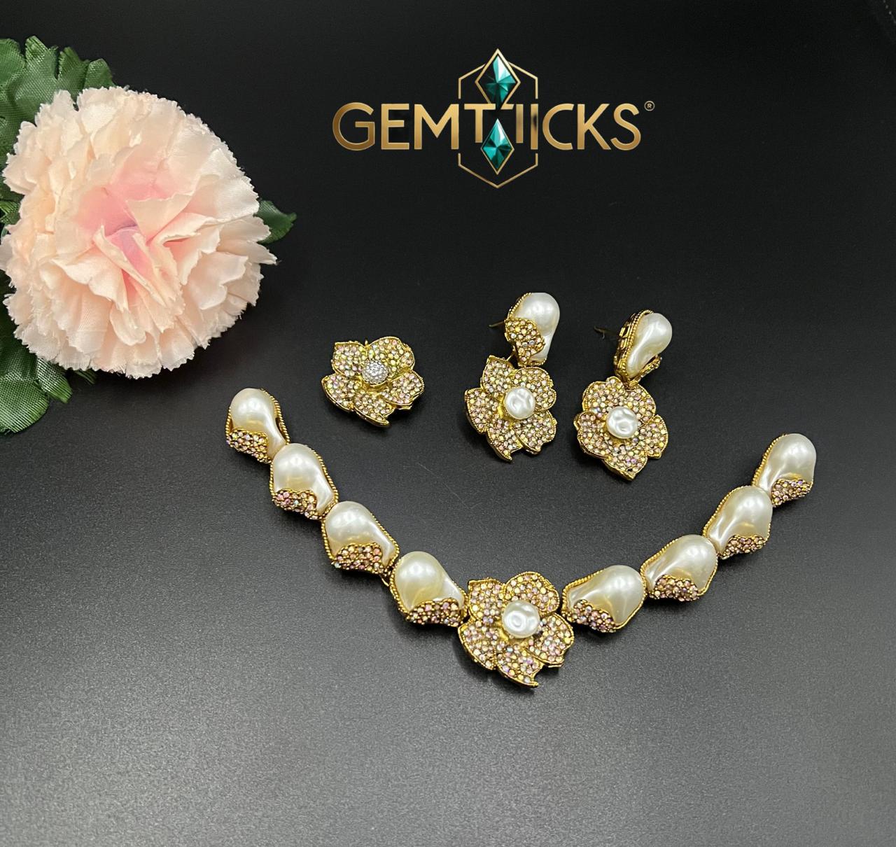 Gold necklace and earrings set with pearls on a dark surface, featuring Gemticks brand logo.