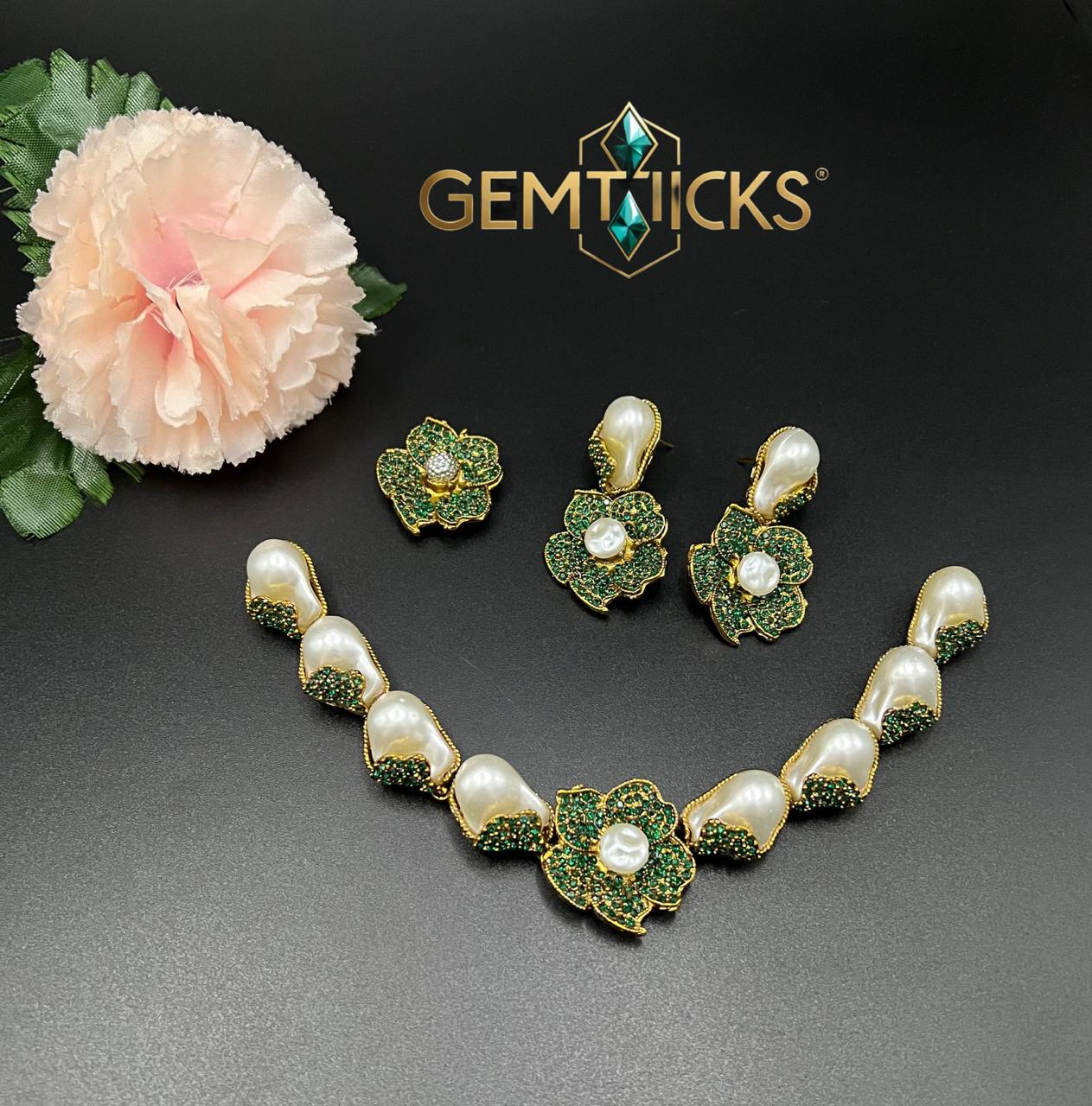 Jewelry set with necklace and earrings on a dark surface with a flower and Gemticks logo.