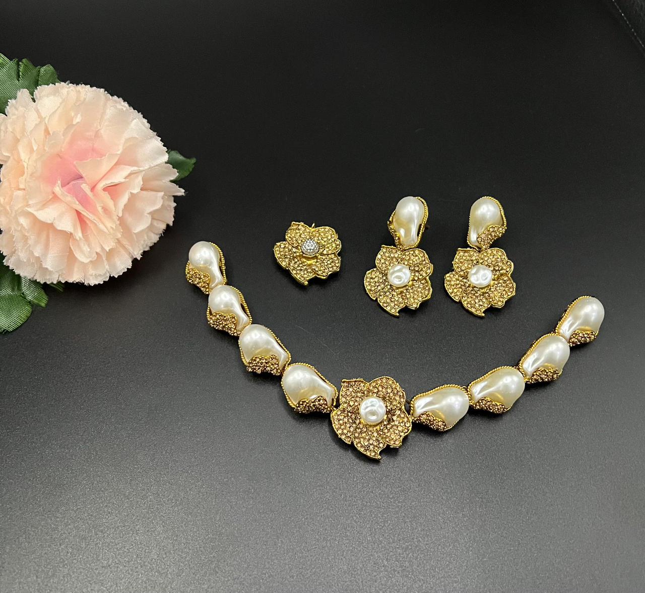 Gold and pearl jewelry set with earrings and necklace on a dark surface with a pink flower.