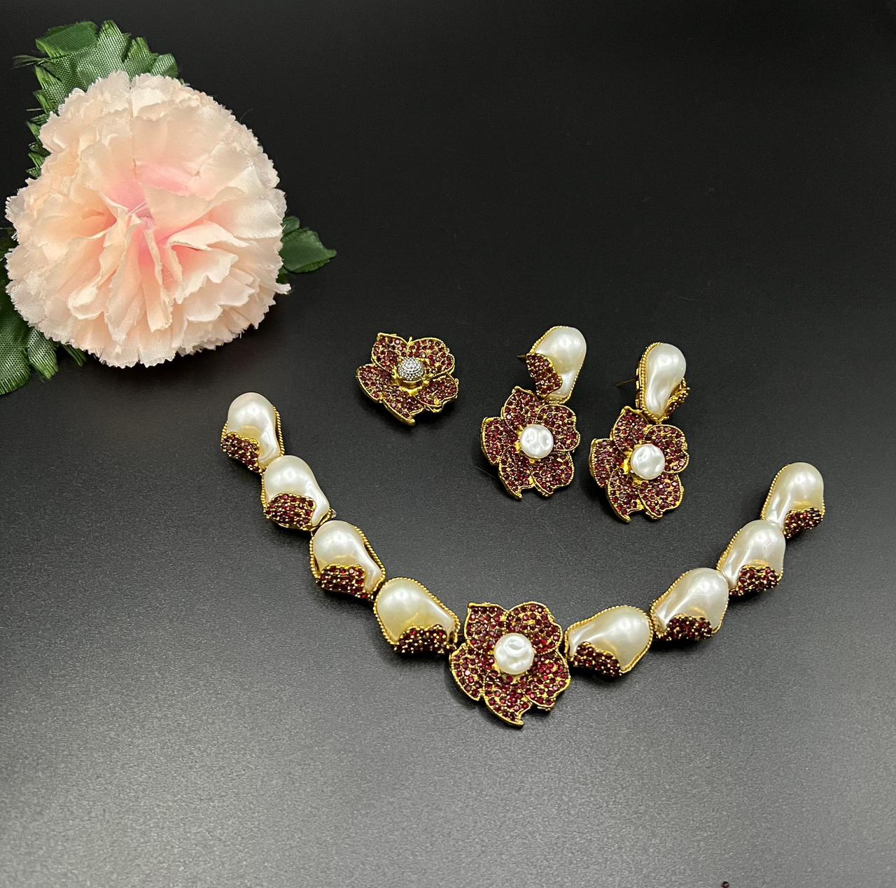 Jewelry set with necklace and earrings on a dark surface with a flower.