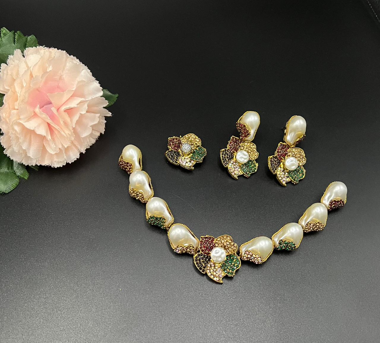 Pearl necklace and earrings with gemstone accents on a dark surface with a flower.