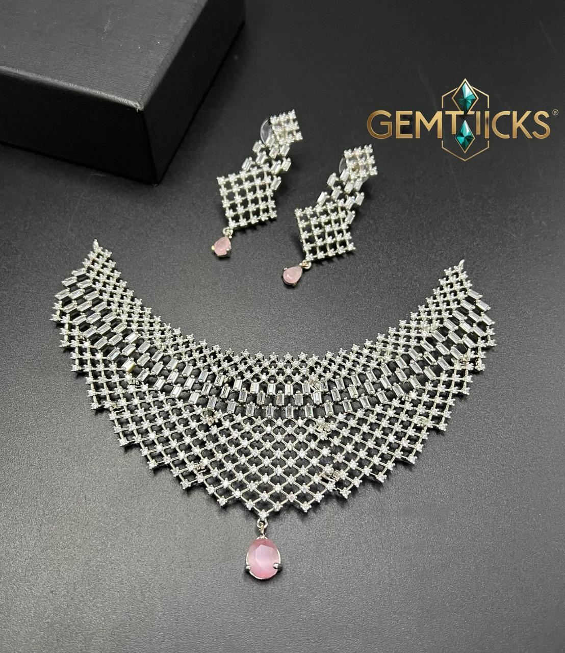 Silver necklace with pink stone and matching earrings on a dark surface, branded 'Gemtlicks'.