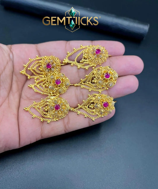 Gold jewelry pieces with red stones held in a hand, brand 'GEMTICKS' visible.