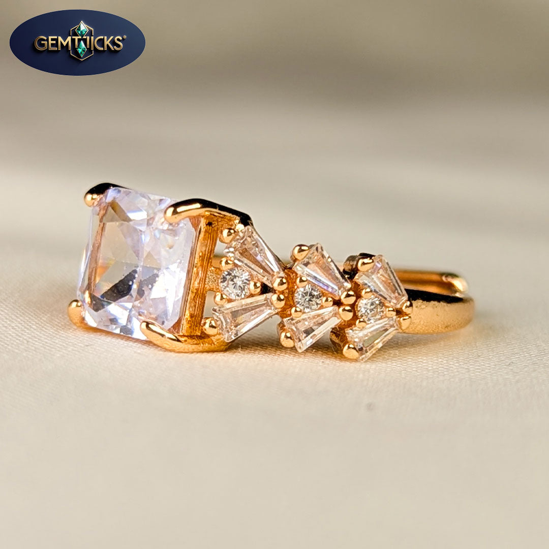 Gold ring with large clear gemstone and smaller baguette-cut stones on a beige background, featuring Gemticks logo.