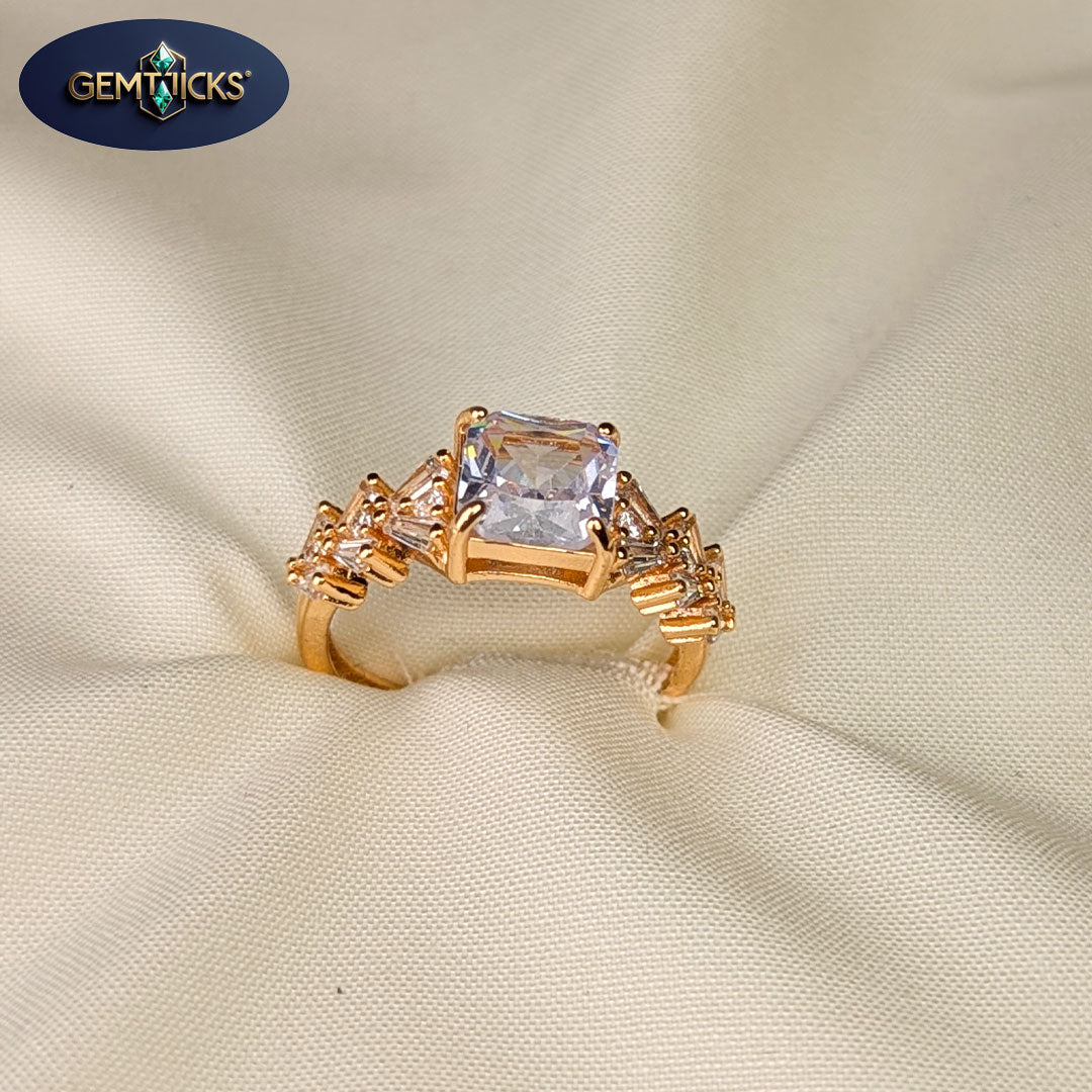 Gold ring with a large central gemstone on a beige fabric background, featuring Gemwicks logo.