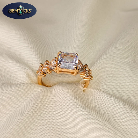 Gold ring with a large central gemstone on a beige fabric background, featuring Gemwicks logo.